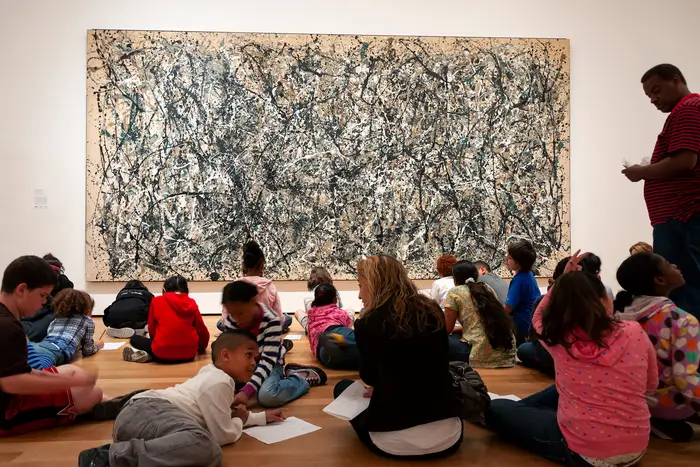 Group of children in a class, sitting in front of a Jackson Pollock painting at the Museum of Modern Art